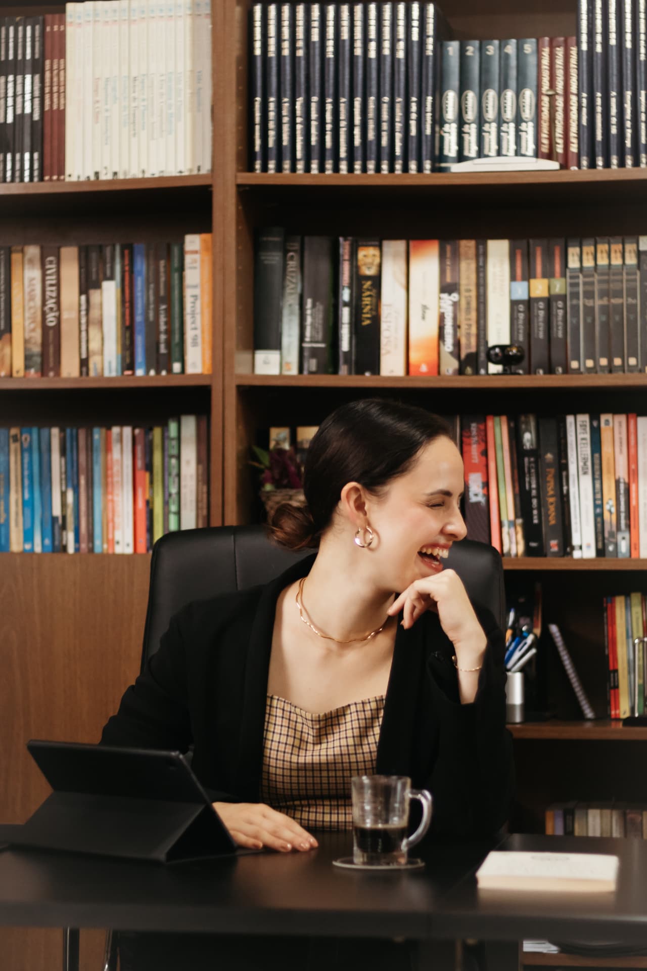 Carolina sorrindo em seu escritório, diante de uma estante de livros